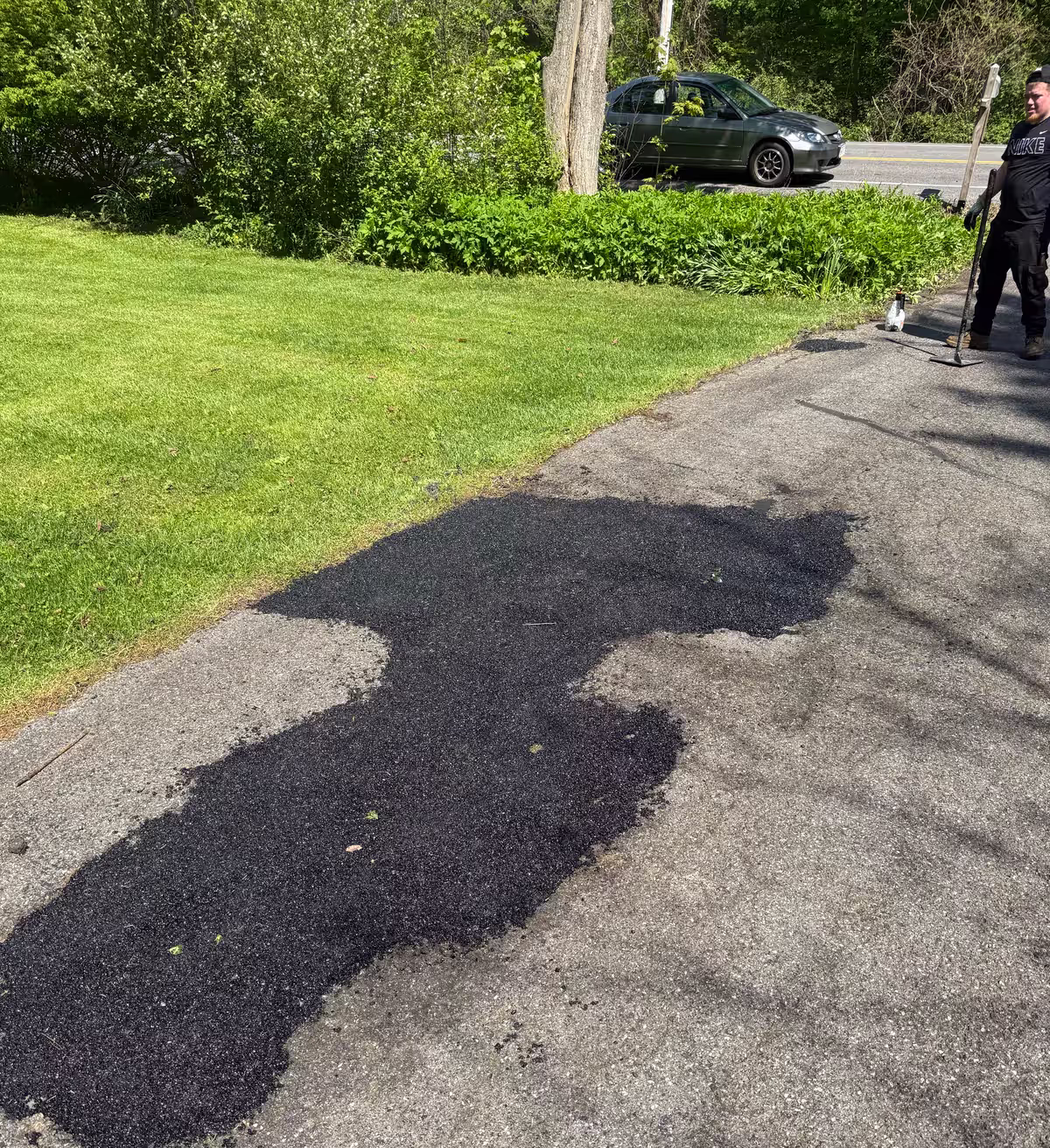 A fresh black asphalt patch laid into a worn gray driveway beside a green lawn