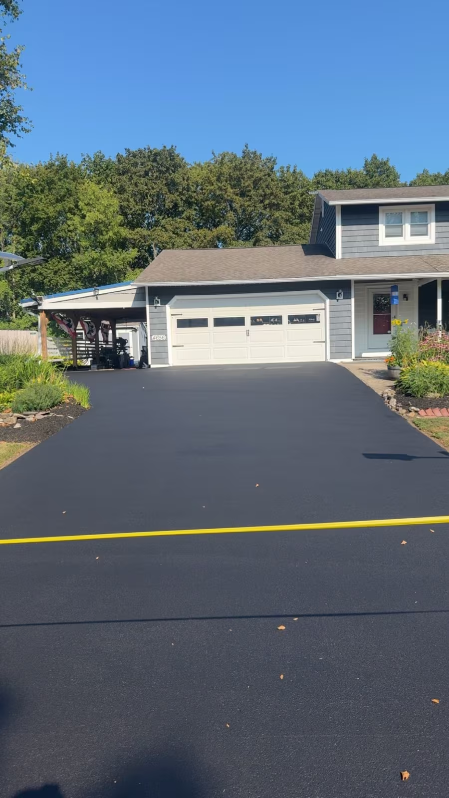 A freshly sealed jet-black driveway running up to a white garage under a clear blue sky