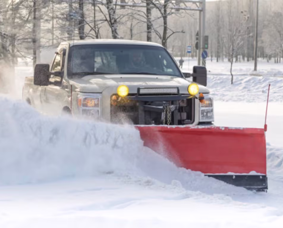 A plow truck with a red blade pushing deep snow off a parking lot