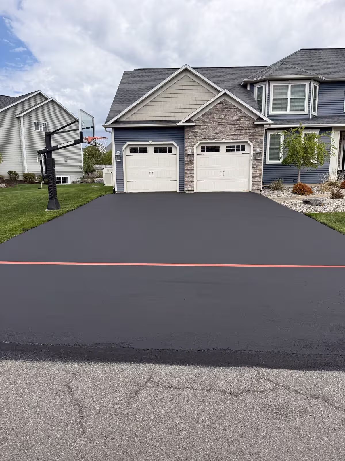 A wide fresh-black asphalt surface edged clean with a crisp red chalk line at a two-story property